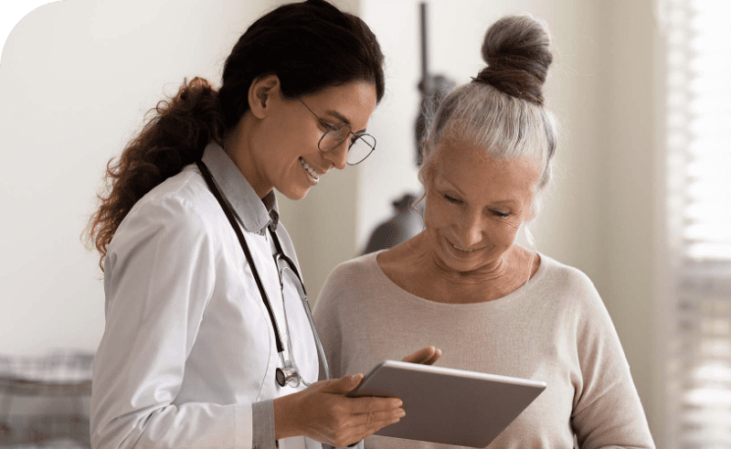 Female doctor reviewing tablet with older woman during medical consultation.