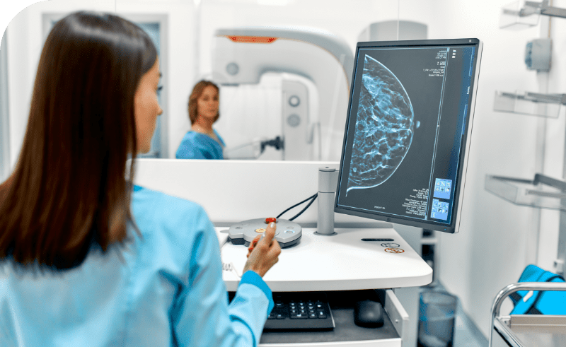 A woman in a hospital room examines a computer screen displaying mammography technology.