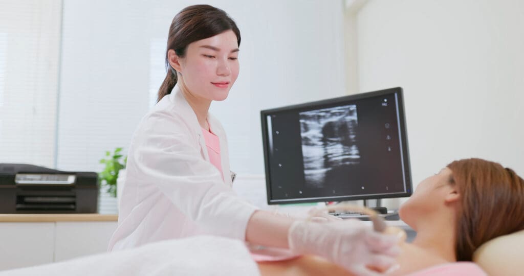 Healthcare provider, wearing medical gloves, is using ultrasound equipment on the breast of a female patient lying down for a screening examination. Medicine concept.