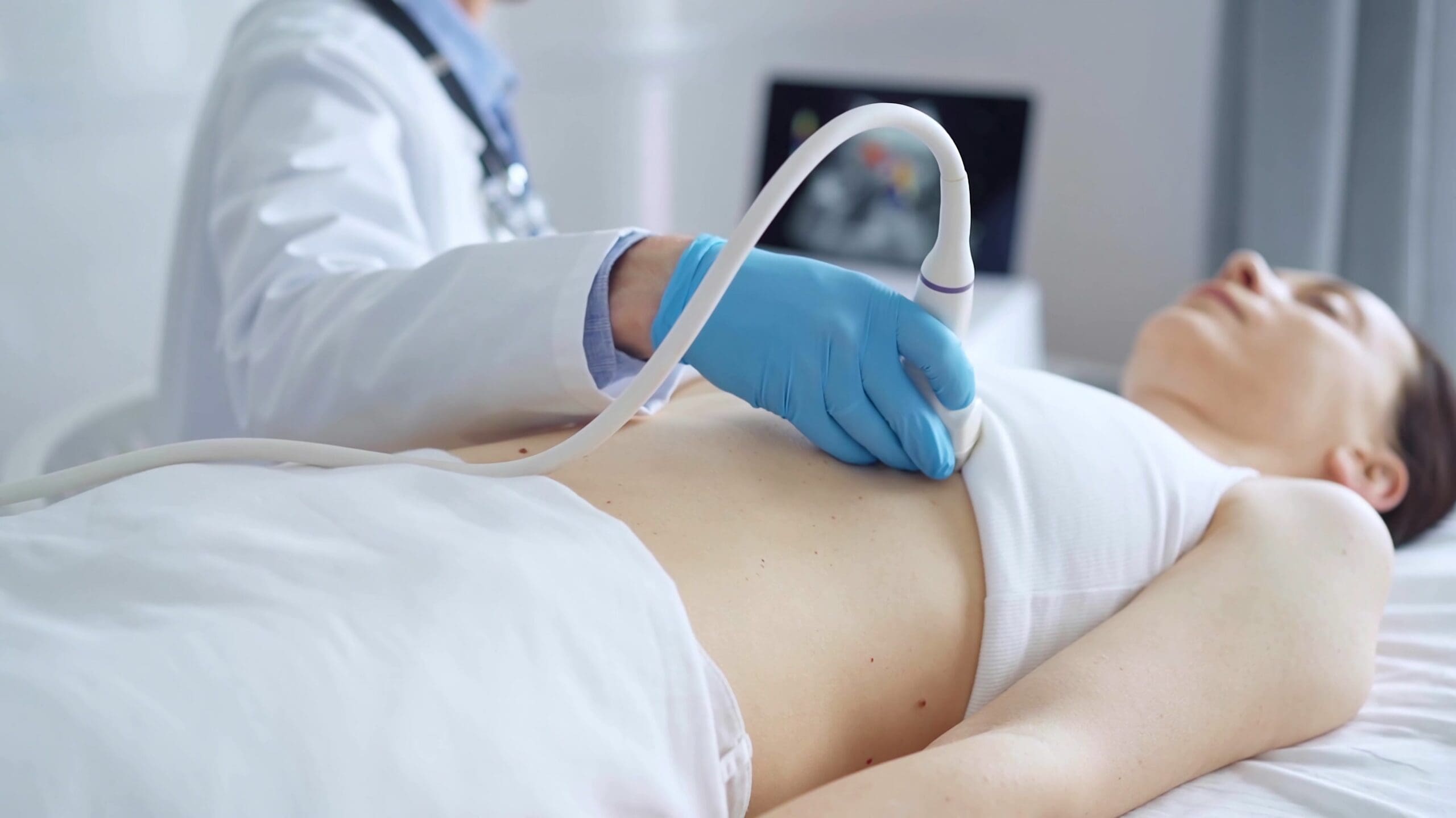 A healthcare provider, wearing blue medical gloves, is using ultrasound equipment on the breast of a female patient lying down for a medical cardiology examination. Medicine concept.